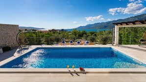 Une piscine avec des chaises longues, une pergola et une vue sur les montagnes et la mer.
