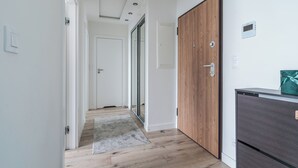 A hallway with wooden flooring, a grey rug, a wooden door, and a dark-colored cabinet. - Langgarten - Little Heaven Apartamenty (Gdansk)