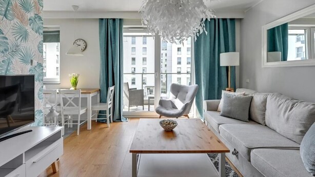 A modern living room with a sofa, a dining table, a TV, and a decorative chandelier. - Langgarten - Little Heaven Apartamenty (Gdansk)