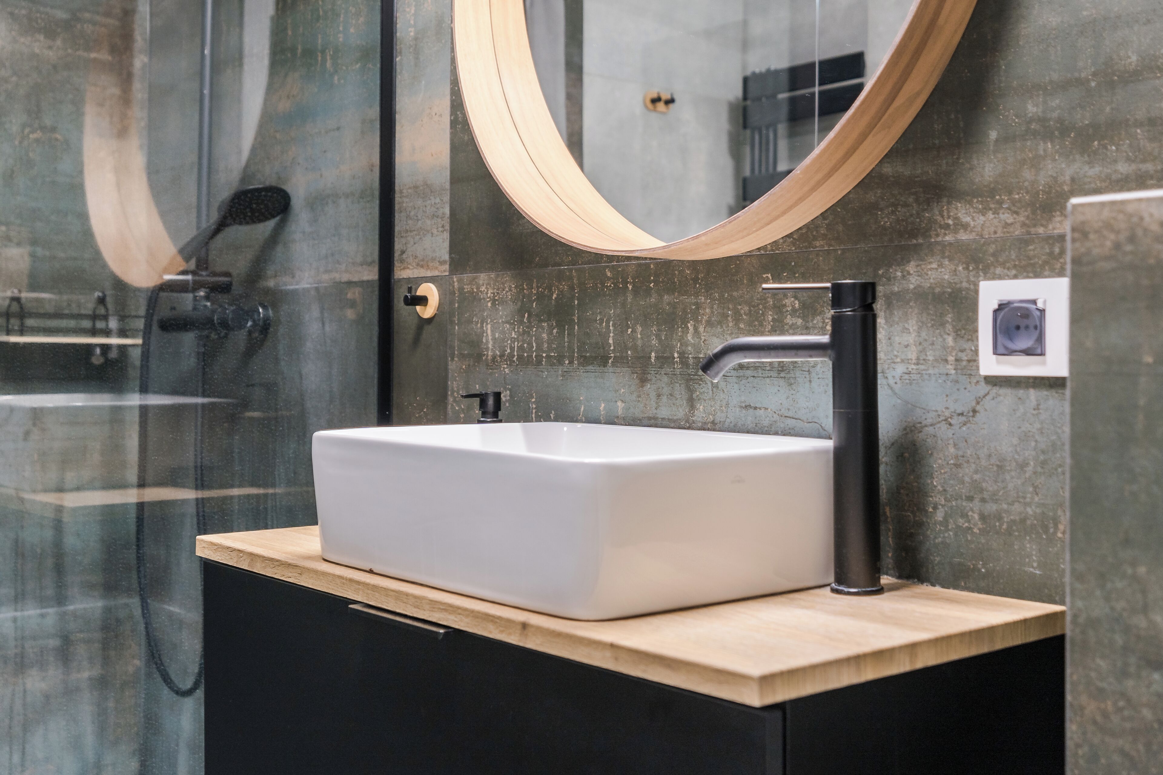 Un baño moderno con un lavamanos blanco, un grifo negro y una encimera de madera.