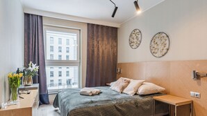 A modern bedroom with a large bed, a bedside table, a small desk, and a window with curtains. - Langgarten - Little Heaven Apartamenty (Gdansk)