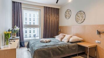 A modern bedroom with a large bed, a bedside table, a small desk, and a window with curtains.