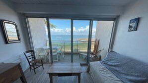 Et værelse med seng, bord og stole, en balkon med havudsigt og et billede på væggen.