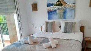 A spacious bedroom with a large bed, a view of the sea, and a balcony.
