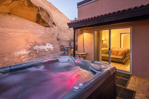 Un jacuzzi installé dans un jardin, avec vue sur une chambre à coucher à travers une porte vitrée.