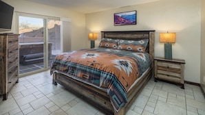 A bedroom with a bed, two bedside tables with lamps, a television on the wall, and a sliding glass door leading to an outdoor area. - Nestled in Towering Slickrock with Private Hot Tub (Moab)