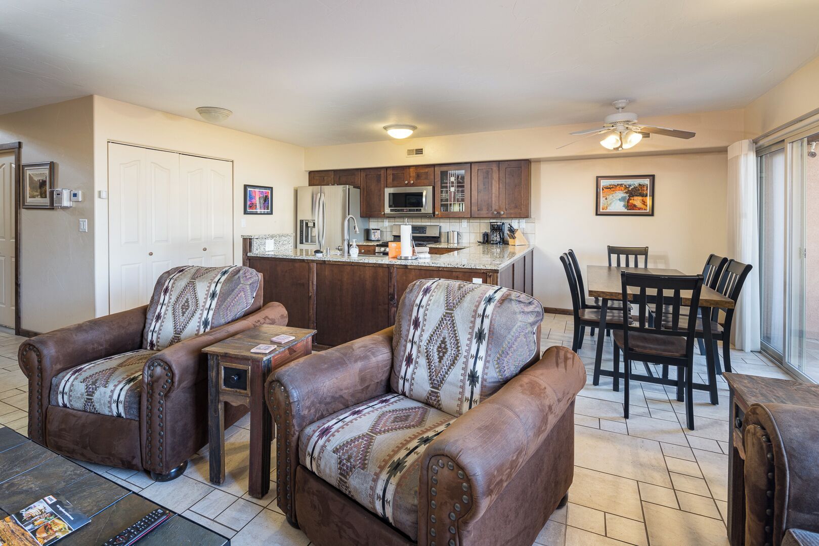 A spacious living room with a fireplace, a dining area with a table and chairs, and a kitchen with wooden cabinets and a refrigerator.