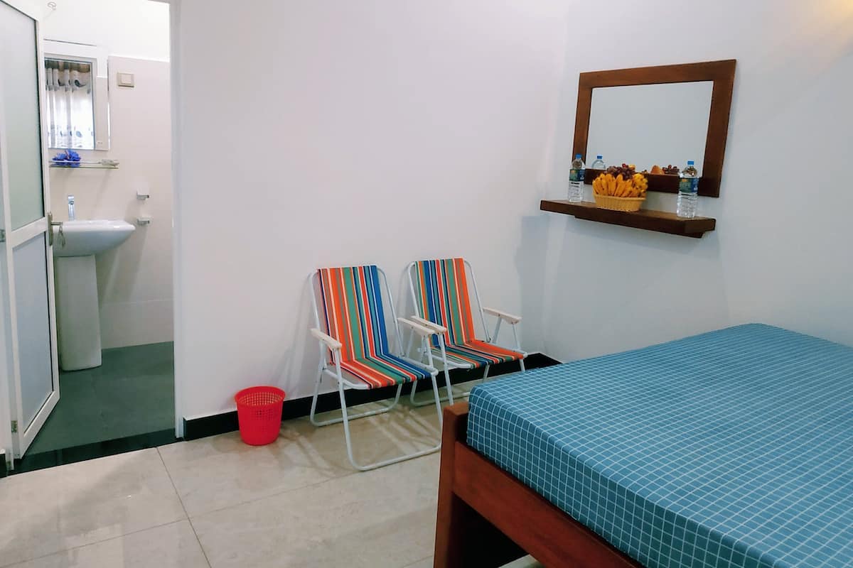 Una stanza con un letto, due poltrone a righe, un tavolino con frutta e acqua, uno specchio e un lavandino.