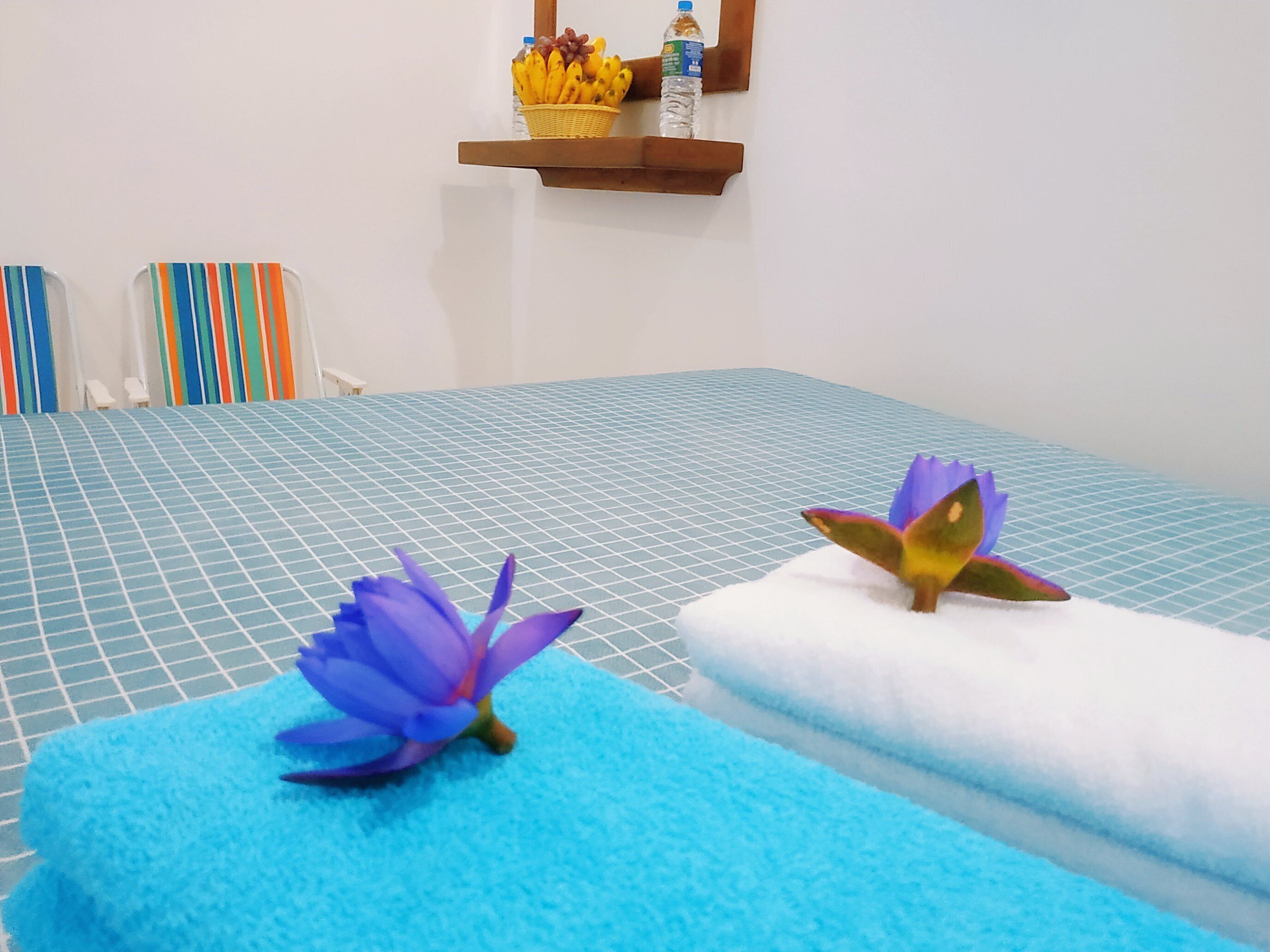 A hotel room with a blue checkered bedspread, a blue bath mat, and two purple lotus flowers on the bed.