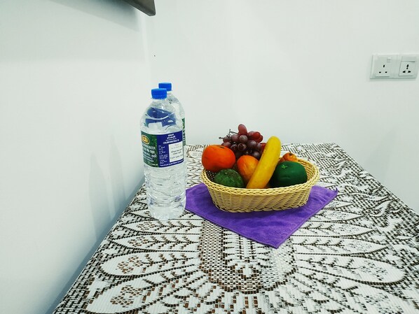 A table with a woven basket containing fruits and a bottle of water.
