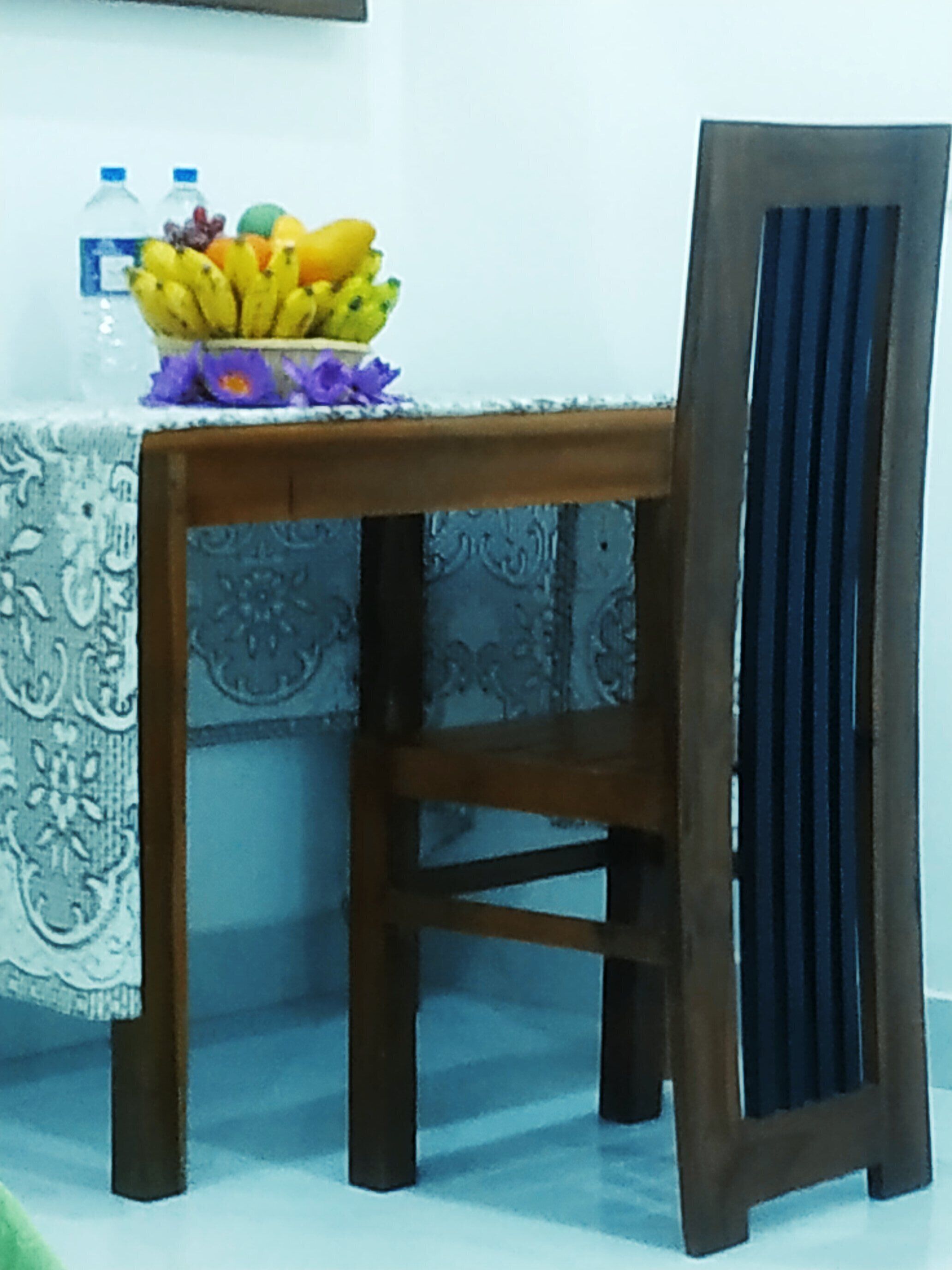 A wooden chair with a dark backrest and a table with a patterned tablecloth.