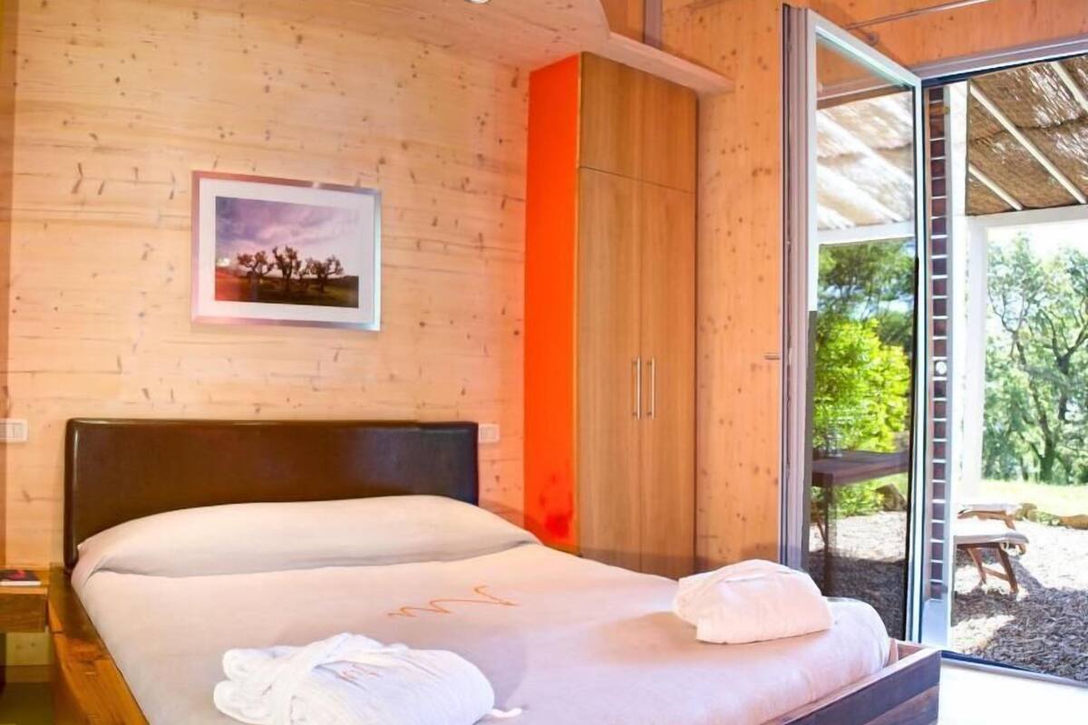 A bedroom with a wooden headboard, a large bed, a framed picture on the wall, and a sliding glass door leading to an outdoor area.