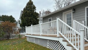 Una terrazza abitativa con ringhiere bianche e una scala in legno che conduce a una casa con rivestimento grigio.