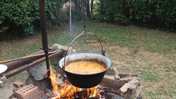 A stone fire pit with a pot of food cooking over an open flame.