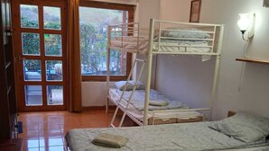 A dormitory room with bunk beds, a desk, and a window with curtains.