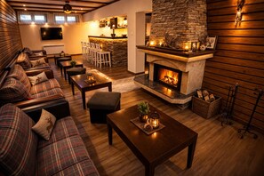 A cozy living room with a fireplace, a sofa set, a dining area, and a kitchen in the background. - Villa Rila in Borovets (Samokov)