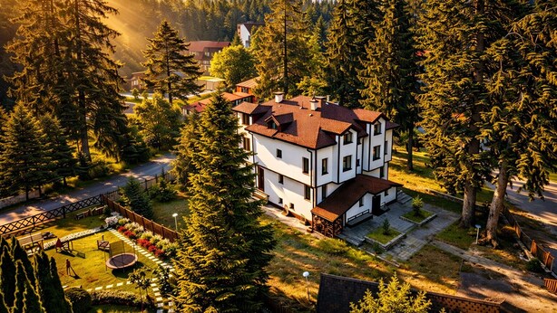 A two-story house surrounded by dense forest, with a well-maintained lawn and a small garden area. - Villa Rila in Borovets (Samokov)