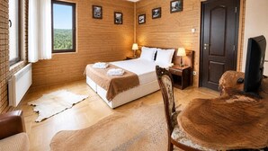 A hotel room with a wooden wall, a large bed, two bedside tables with lamps, a television, and a view of the outdoors. - Villa Rila in Borovets (Samokov)