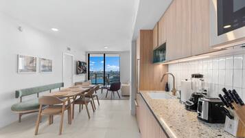 A modern kitchen with a granite countertop, a built-in oven, and a sink. There is a dining area with a table and chairs, and a bench along the wall.