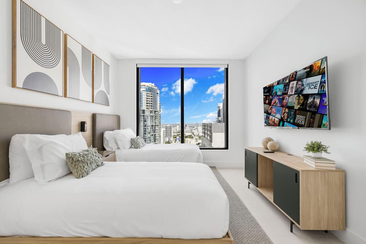 A modern bedroom with a large window, a bed, a bedside table, and a TV wall art.
