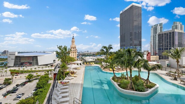 A rooftop pool area with palm trees, a modern building, and a historic tower. - Luxury Condos in Downtown Miami (Miami)