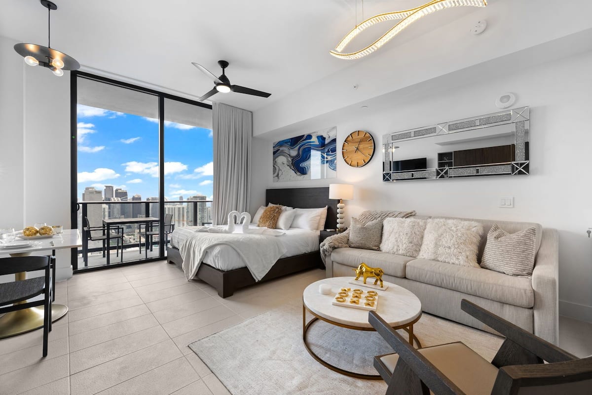 A modern bedroom with a city view, a balcony, and a living area with a sofa and coffee table.