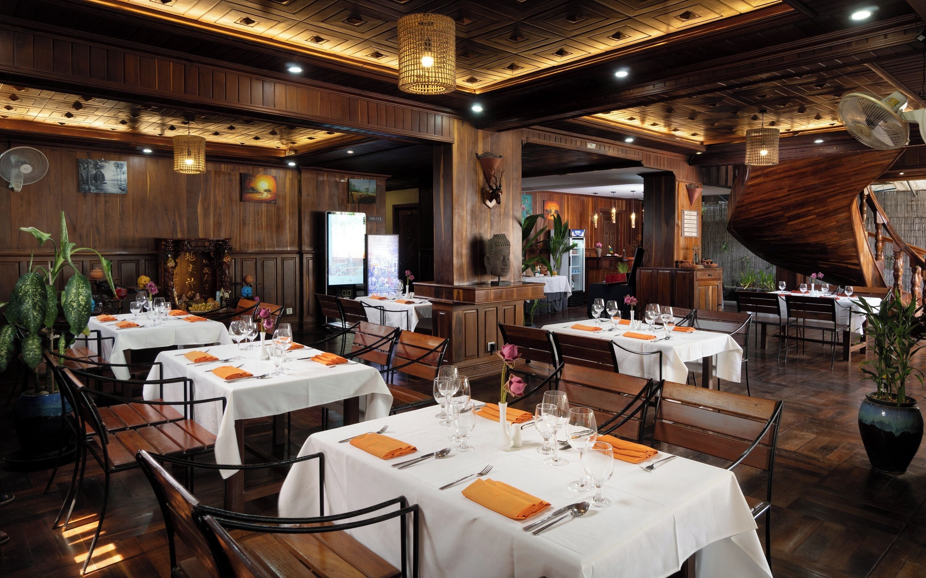 A restaurant with multiple tables set for dining, wooden paneling on the walls, and a staircase leading to an upper level.