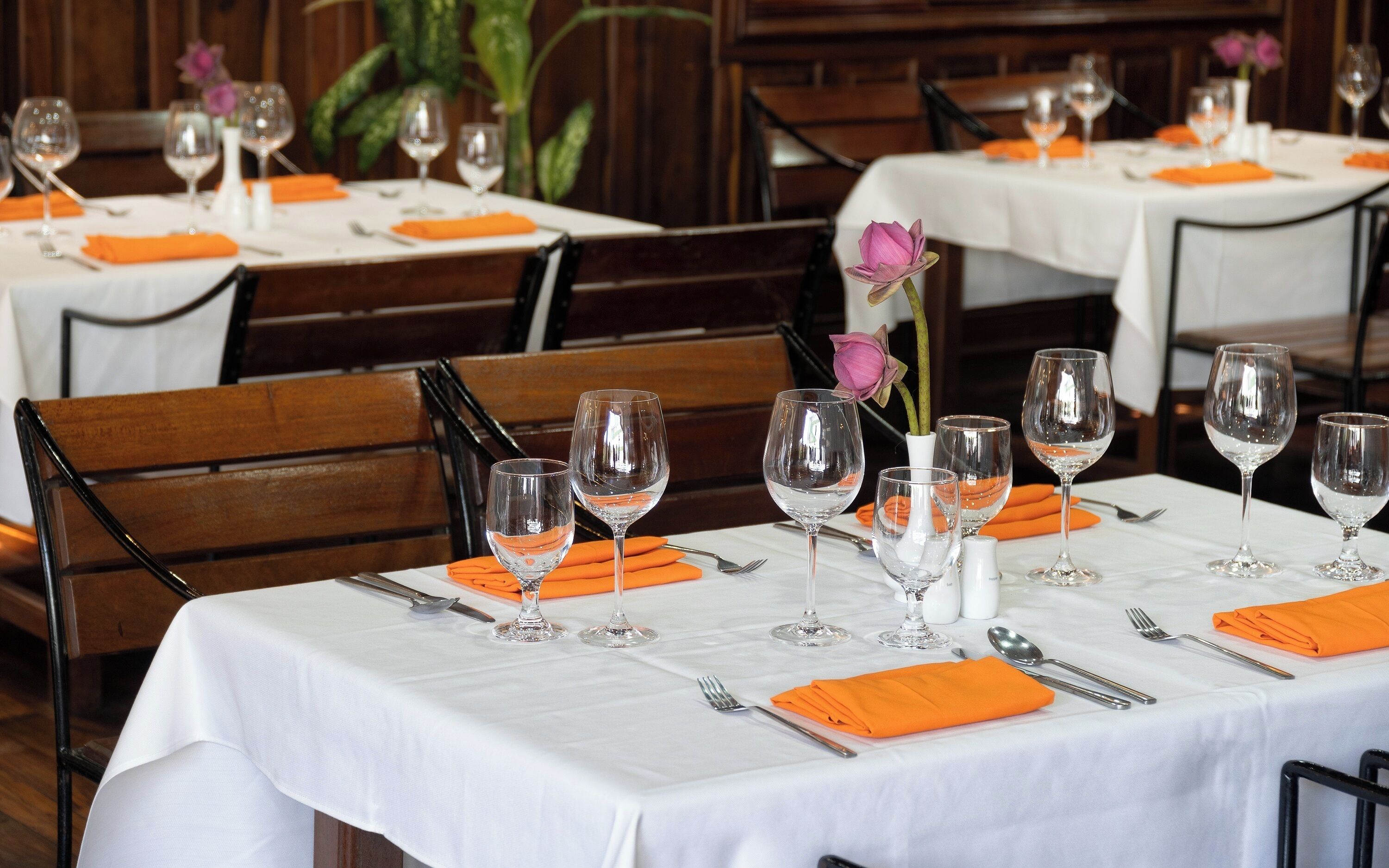 A restaurant with tables set for dining, featuring white tablecloths and orange napkins.