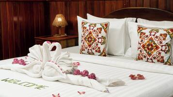 Een netjes opgemaakt bed met een handdoek gevouwen in de vorm van een zwaan, kussens met bloemenmotieven en een bord met de tekst 'WELCOME' op het bed.