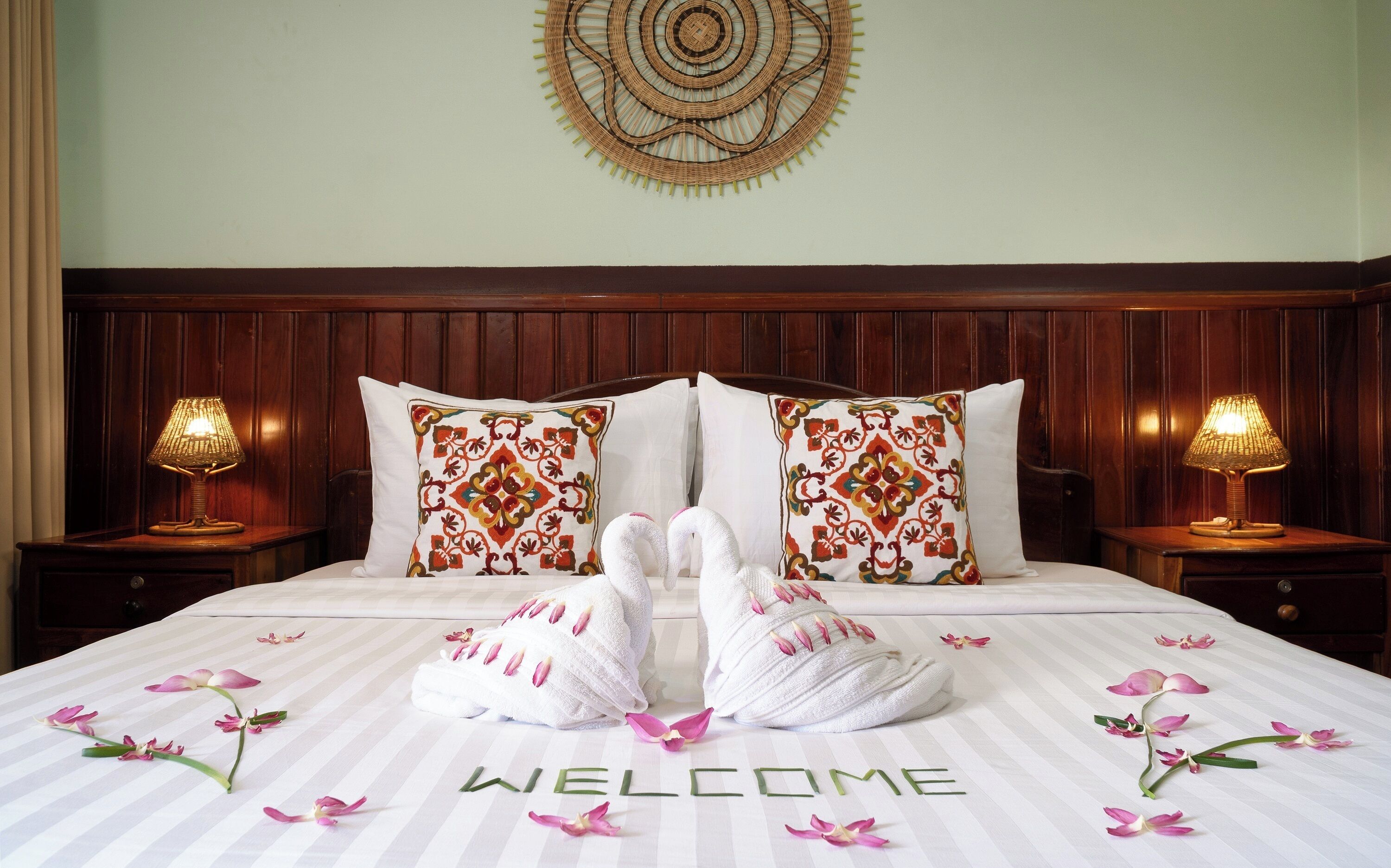 A neatly made bed with a "WELCOME" sign, two decorative pillows, and a wall hanging.
