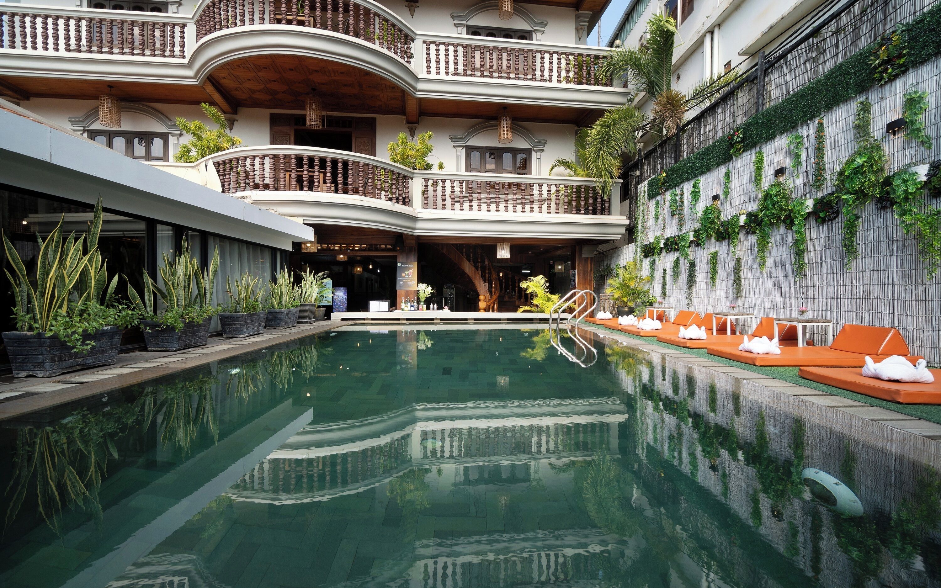 A pool area with a reflection, potted plants, and a seating area with cushions.