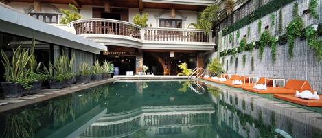 A pool area with a reflection, potted plants, and a seating area with cushions.
