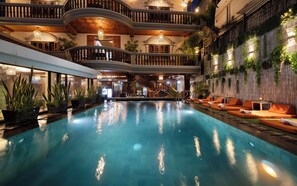 An indoor swimming pool with a central staircase, lounge areas with orange seating, and a decorative wall with plants. - Siem Reap Center Hotel (Siem Reap)