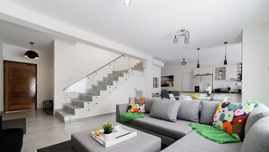 A modern living room with a grey sofa, a coffee table with a tray, and a staircase leading to a kitchen area.