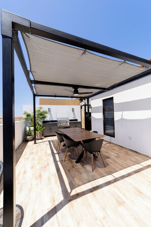 An outdoor patio with a table and chairs, a grill, and potted plants.