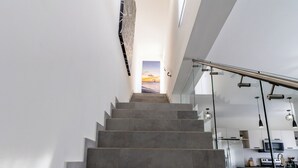 A modern staircase leading to a kitchen area with a glass railing and a view of the outdoors.