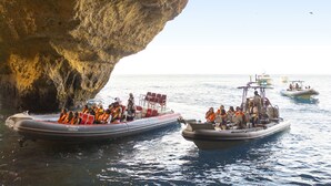 L'ingresso di una grotta con barche ormeggiate all'interno, passeggeri con salvagente e vista chiara sul mare.