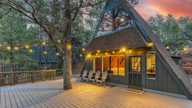 A cozy cabin with a wooden deck, two Adirondack chairs, and a large window overlooking the forest.