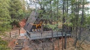 A rustic cabin with a wooden deck, surrounded by trees.