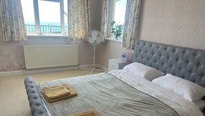 A bedroom with a bed, a radiator, a window with curtains, a bedside table, and a potted plant. - Brighton - 3 Beds - Pet Friendly - Sea View (Brighton)