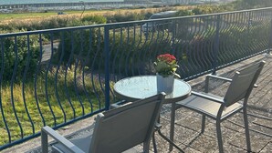 A balcony with a glass table and chairs, a vase with flowers, and a view of the sea and buildings. - Brighton - 3 Beds - Pet Friendly - Sea View (Brighton)