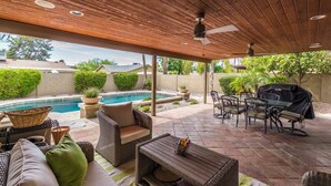 A covered patio with a pool, outdoor furniture, and a grill area.