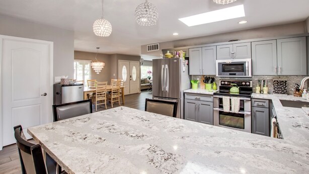 A modern kitchen with marble countertops, stainless steel appliances, and pendant lighting.