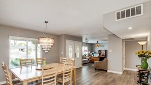 A spacious dining area with a wooden table and chairs, a chandelier, and a view of the outdoors through large windows.