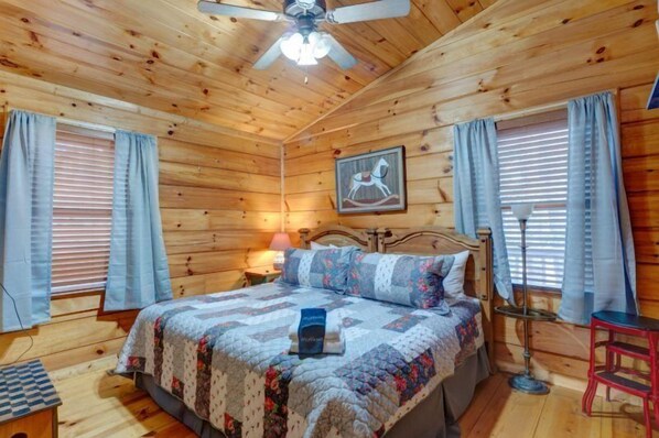 A wooden cabin bedroom with a bed, curtains, a ceiling fan, and a framed picture on the wall. - Dancing Bear-Blue Ridge GA (Blue Ridge)