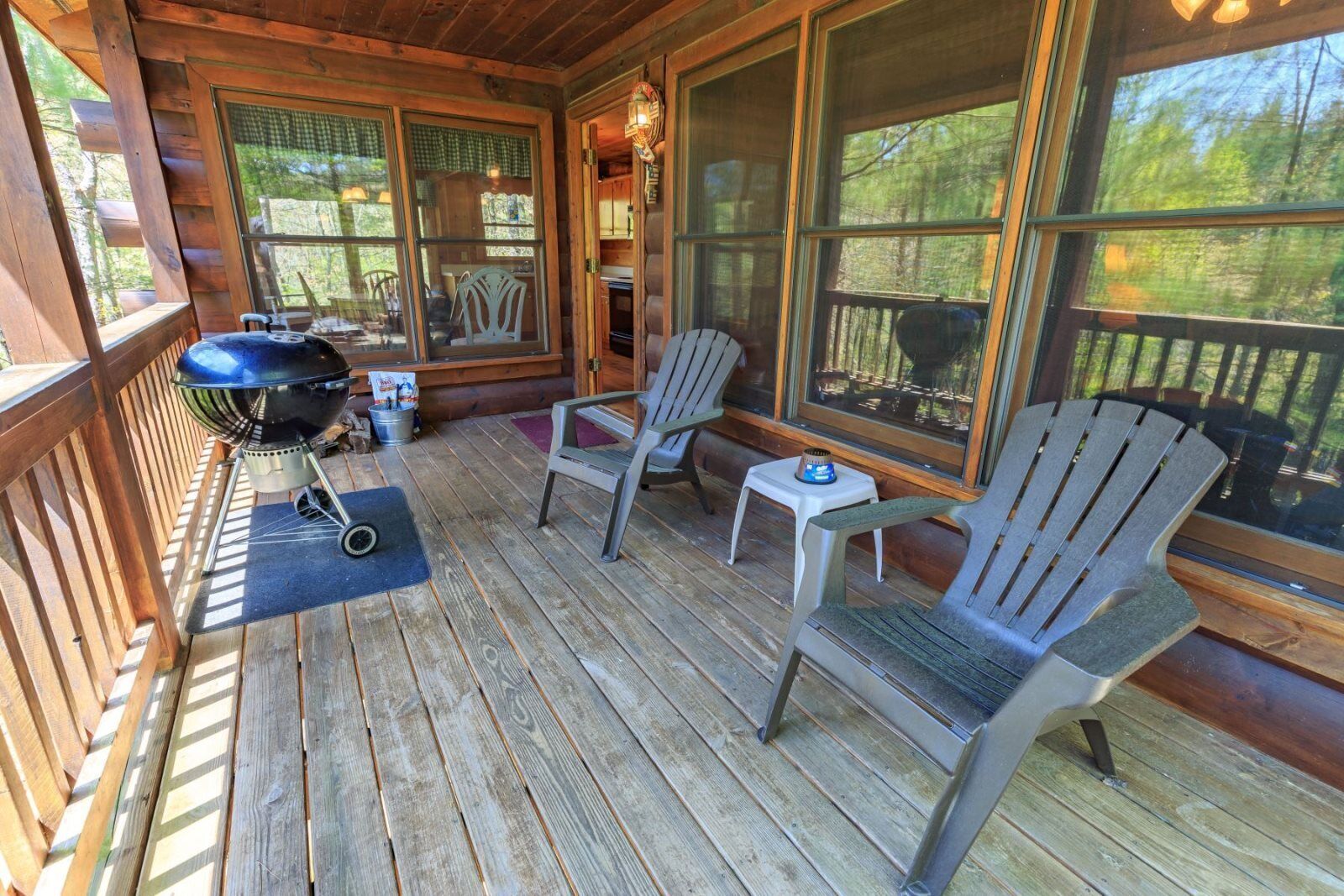 Une terrasse en bois avec des fauteuils Adirondack, un barbecue et de grandes fenêtres donnant sur le paysage extérieur.