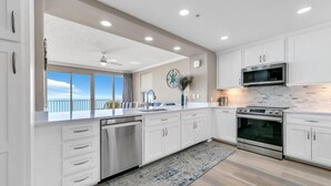 A modern kitchen with white cabinets, stainless steel appliances, and a large window offering a view.
