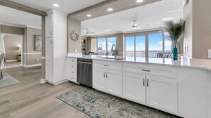A modern kitchen with white cabinetry, a dishwasher, and a large window offering a view of the outdoors.