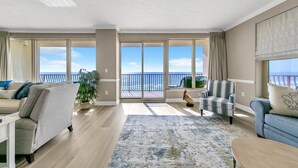 A spacious living room with a large sliding glass door leading to a balcony with a view of the ocean.
