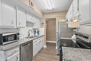 A modern kitchen with white cabinetry, stainless steel appliances, and a granite countertop. - 🌴 Winter Deal ❄️ Golf Cart-Heated Pool-FAB Reno- Seascape 22A🌊 (Miramar Beach)